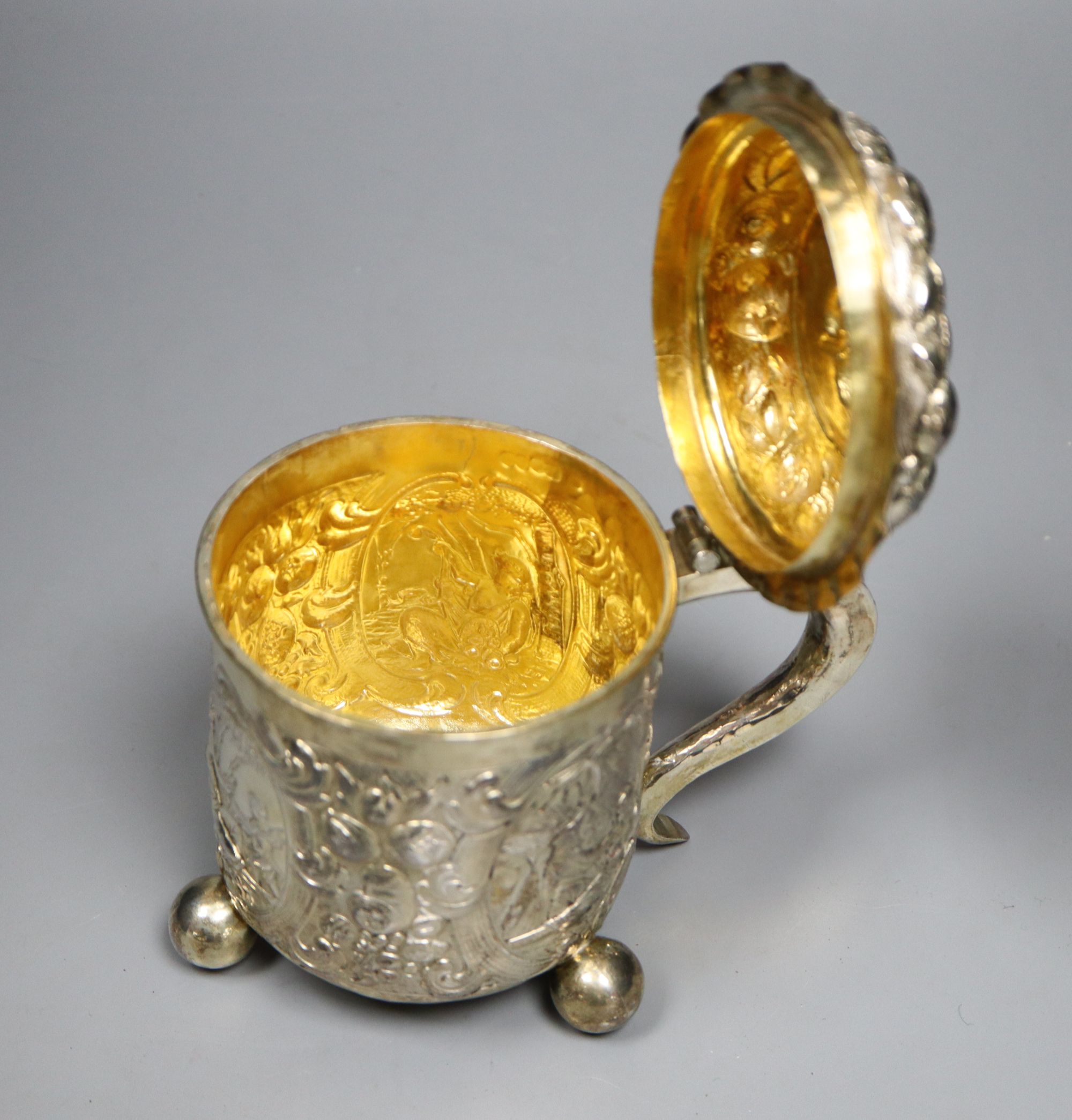 A late 19th century German? silver Scandinavian style embossed lidded tankard, on three ball feet,